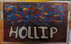 A cassette with the word HOLLIP painted on it. There is red and blue paint across the front.